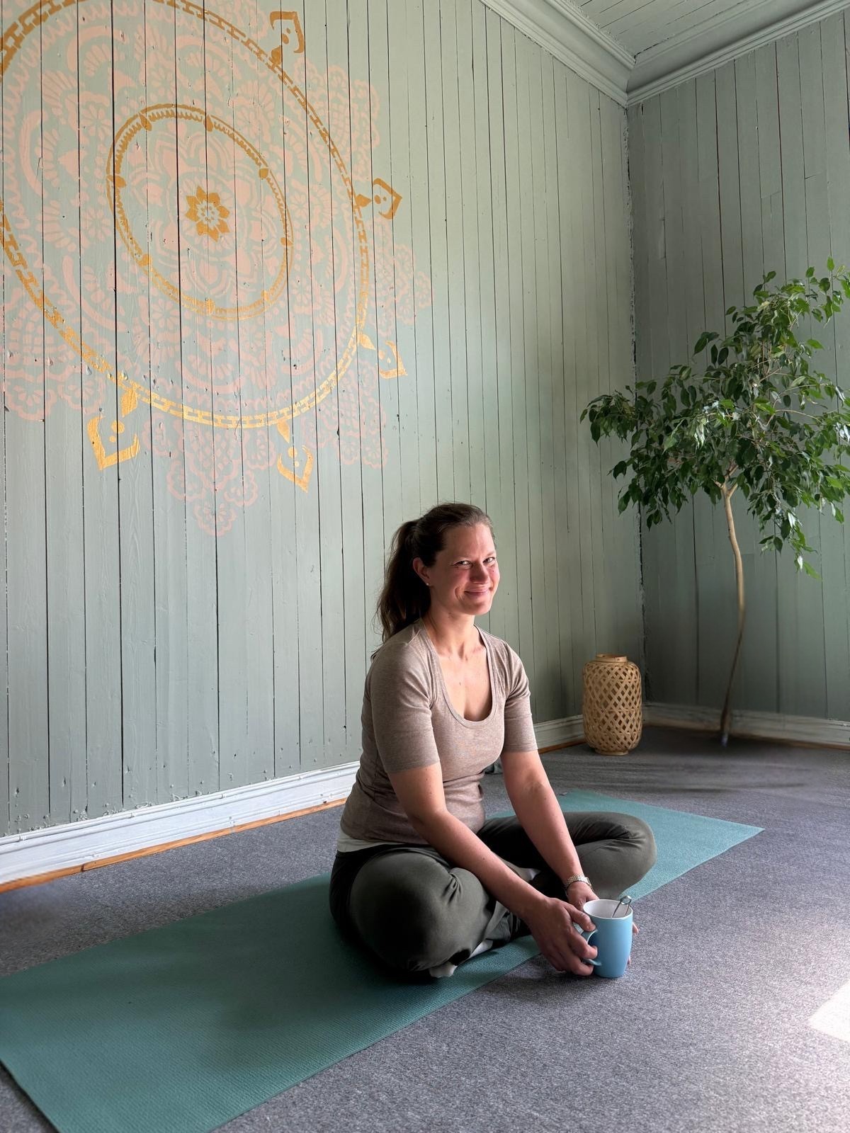 Eline sitter på yogamåtte i praksisrommet med mandala på veggen